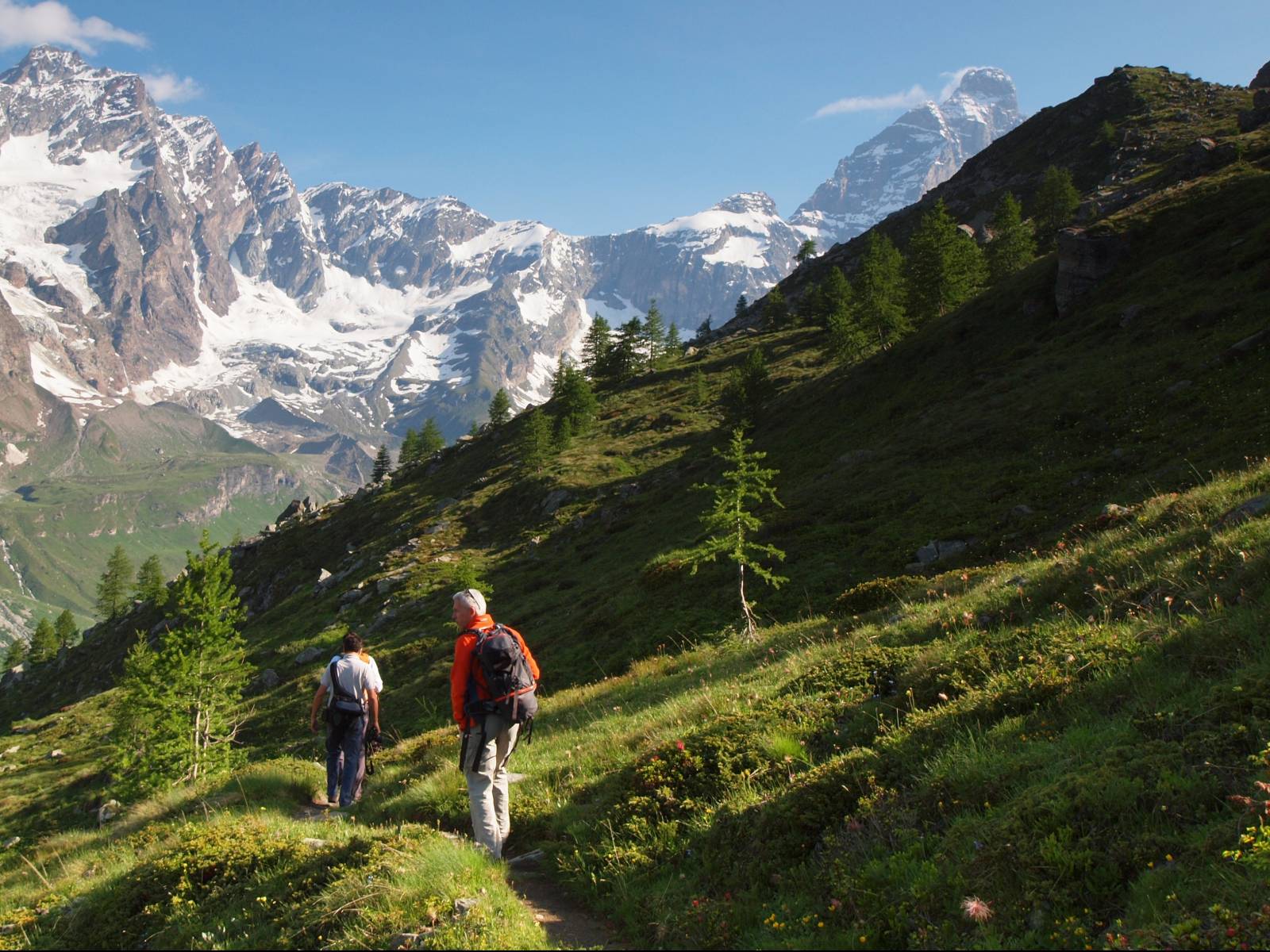 Escursionisti lungo un sentiero di trekking a Cervinia con vista sulle vette alpine e sul Monte Cervino, immersi nei paesaggi naturali della Valle d'Aosta.