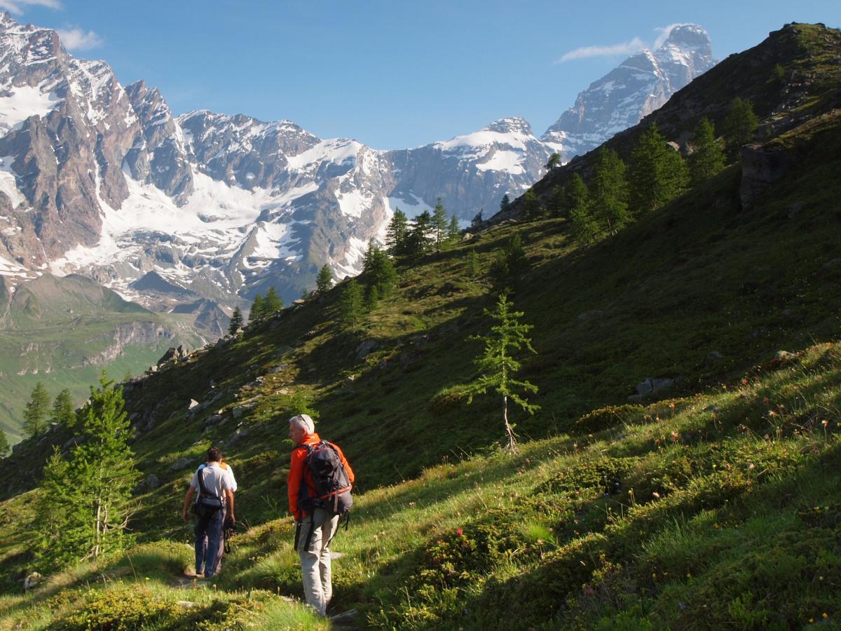 Escursionisti lungo un sentiero di trekking a Cervinia con vista sulle vette alpine e sul Monte Cervino, immersi nei paesaggi naturali della Valle d'Aosta.